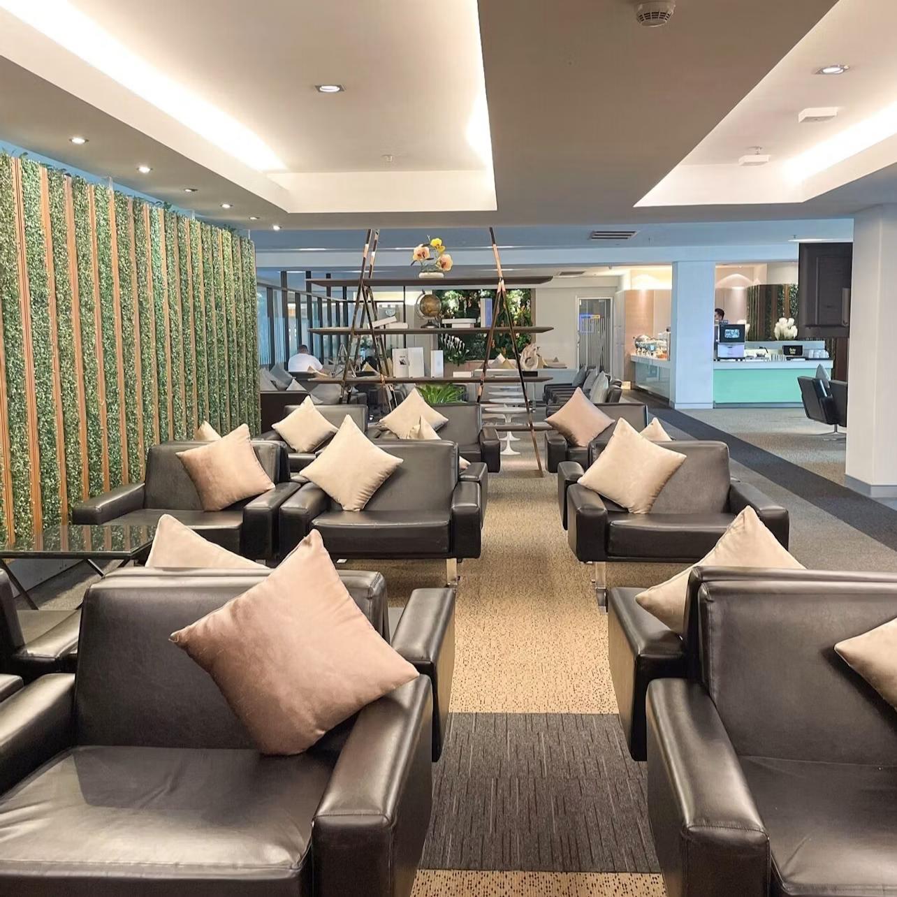 A modern lounge area with black armchairs, beige cushions, and decorative plants under warm ceiling lighting.