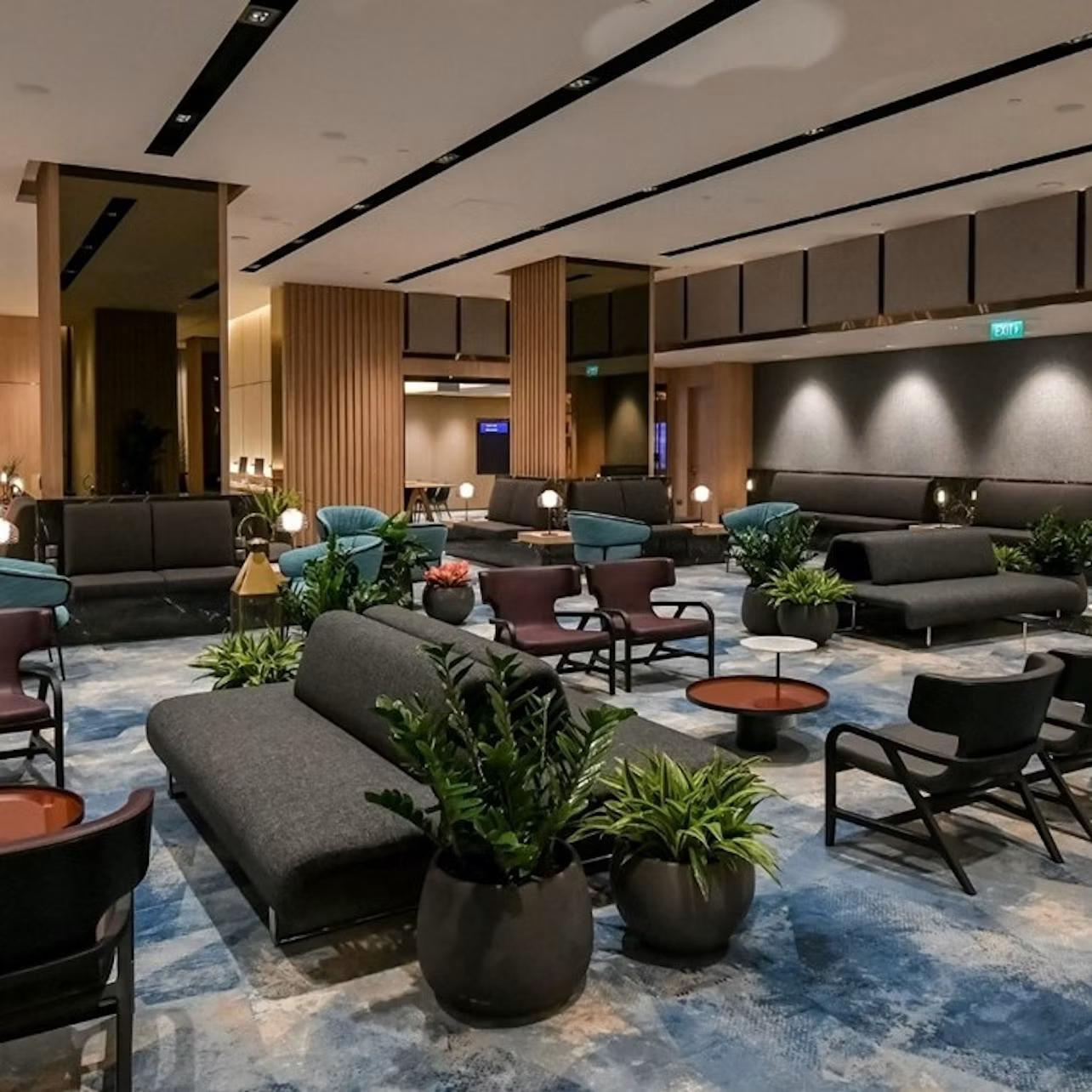 A modern lounge area with sofas, armchairs, coffee tables, and potted plants, featuring warm lighting and a contemporary design.